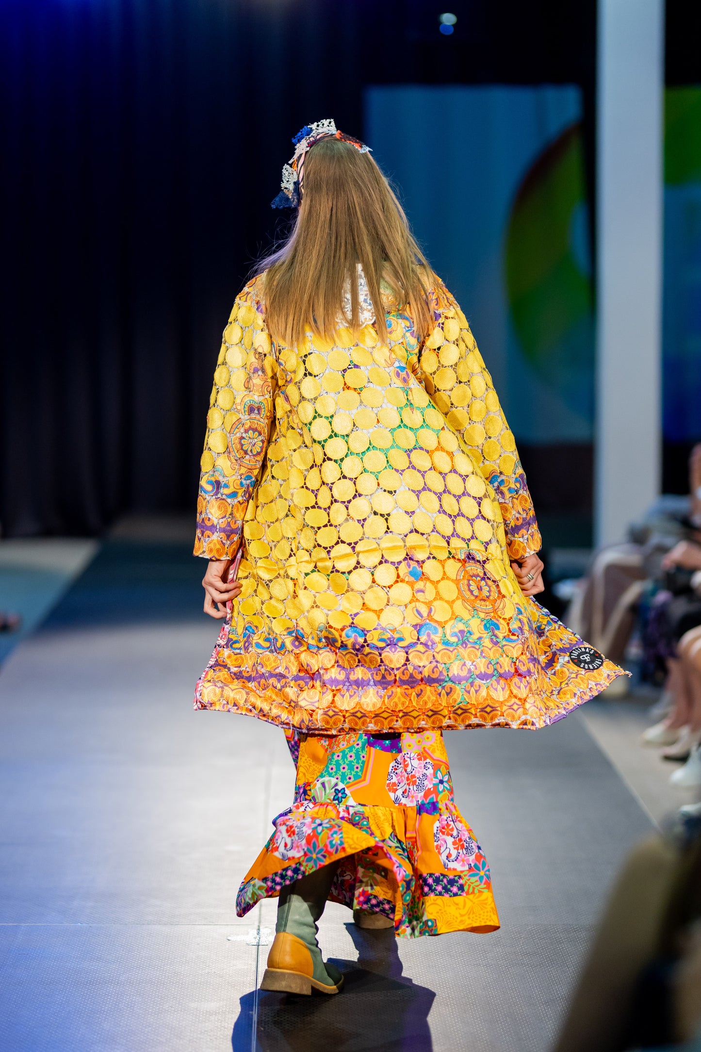 Close-up view of a vibrant, intricately designed fabric detail from an upcycled vintage kimono-style coat. Features bold yellow lace patterns, colorful floral embroidery, and a mix of rich, festive prints inspired by Canarian carnival aesthetics. A striking combination of textures and colors for a unique, eye-catching garment.