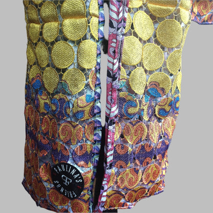 Close-up view of a vibrant, intricately designed fabric detail from an upcycled vintage kimono-style coat. Features bold yellow lace patterns, colorful floral embroidery, and a mix of rich, festive prints inspired by Canarian carnival aesthetics. A striking combination of textures and colors for a unique, eye-catching garment.
