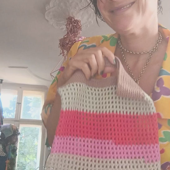 Hand-crocheted tote bag with multicolored horizontal stripes in shades of beige, blue, pink, and red, featuring an integrated handle and open-weave design.