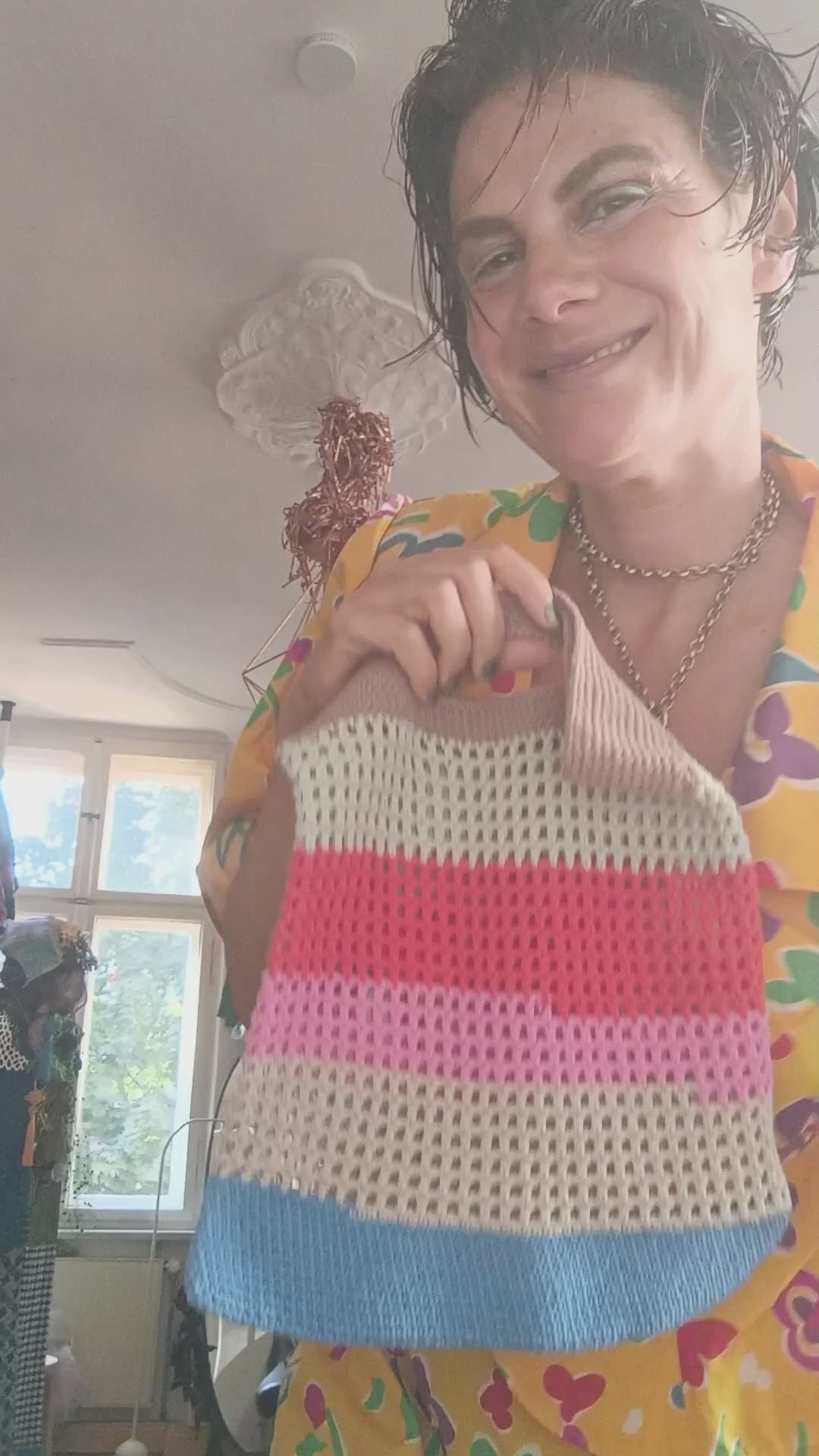 Hand-crocheted tote bag with multicolored horizontal stripes in shades of beige, blue, pink, and red, featuring an integrated handle and open-weave design.